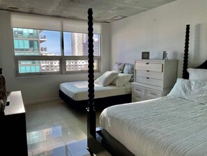 Relax in a serene bedroom with a four-poster bed and a second bed, offering a city view through a large window.