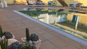 Uma área de piscina com piso em azulejo, plantas em vasos e mobiliário de exterior.