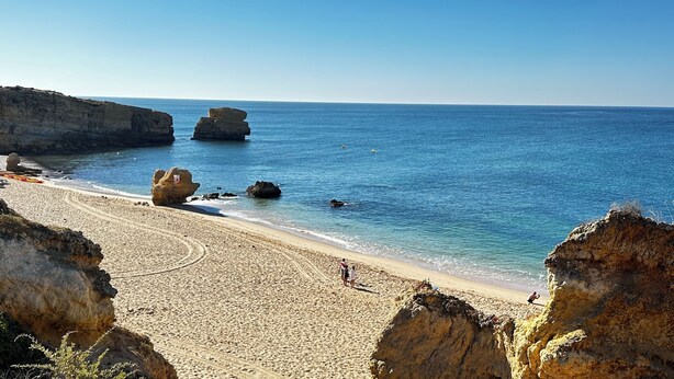 Uma praia com águas azul-claras, formações rochosas e uma orla arenosa.