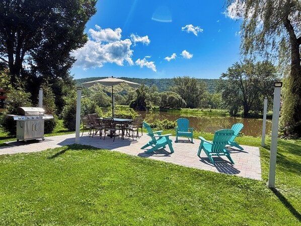 An outdoor patio with a grill, table, chairs, and a view of a lake and hills. - Beau Rivage Waterfront, kayak, SUP, great fishing, swimming, fire pit, updated (Portlandville)