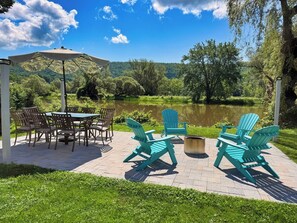 An outdoor patio with a table and chairs, a fire pit, and a view of a lake and forest.