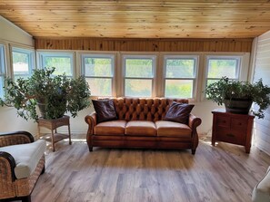 A room with a leather sofa, wooden flooring, a wooden ceiling, and large windows. - Beau Rivage Waterfront, kayak, SUP, great fishing, swimming, fire pit, updated (Portlandville)