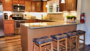 A modern kitchen with wooden cabinets, stainless steel appliances, a central island with bar stools, and pendant lighting. - Beau Rivage Waterfront, kayak, SUP, great fishing, swimming, fire pit, updated (Portlandville)