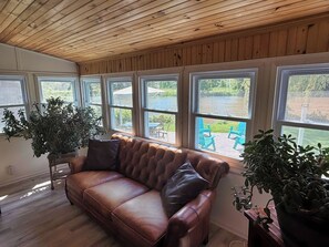 A room with a brown leather sofa, large windows, and potted plants.