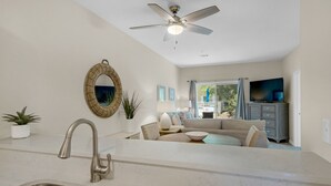A modern kitchen with a sink and faucet, a dining area with a table and chairs, a sofa, and a television. - Walkable to Dining, Shopping, Beach | Sleeps 6 | Free Bike Rentals + More! (Santa Rosa Beach)