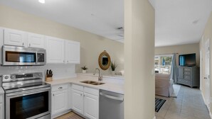 A modern kitchen with white cabinets, stainless steel appliances, a microwave, oven, and dishwasher. There is a sink with a faucet, a decorative mirror, and a potted plant. - Walkable to Dining, Shopping, Beach | Sleeps 6 | Free Bike Rentals + More! (Santa Rosa Beach)
