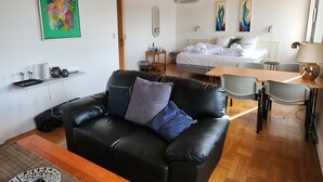 Een moderne woonkamer met een zwarte leren bank, een houten salontafel, en een eethoek met een tafel en stoelen.