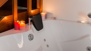 Una bañera blanca con un asiento negro, rodeada de velas y vigas de madera en el techo.