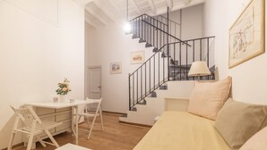 Un dormitorio con una cama, un escritorio y una silla. Se ve una escalera con barandilla que conduce a un nivel superior.