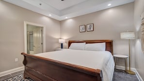 A bedroom with a large wooden bed, a bedside table with a lamp, a floor lamp, and two framed wall art pieces.