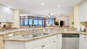 Una cocina moderna con encimeras de granito, muebles blancos, un lavamanos de acero inoxidable y lavavajillas integrado.
