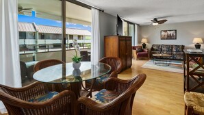 Un amplio salón con una mesa de vidrio rodeada de sillones de mimbre, un sofá y un televisor.