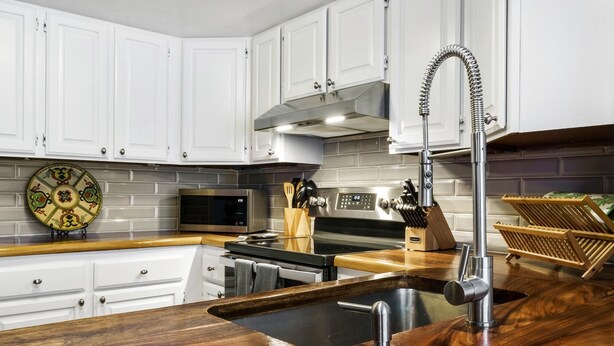 Una cocina moderna con armarios blancos, una campana extractora de acero inoxidable, un microondas y una encimera de madera con fregadero.