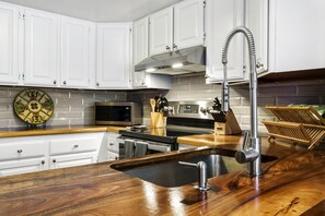 Une cuisine moderne avec des armoires blanches, une hotte en acier inoxydable, un four à micro-ondes et un plan de travail en bois doté d’un évier.