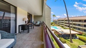 Un balcón con vista a una piscina y palmeras, amueblado con sofá, mesa y sillas.