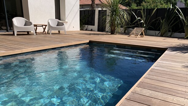 Piscina cristalina con plataforma de madera y sillones de descanso blancos.