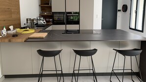 Una cocina moderna con una isla central, dos taburetes de bar y electrodomésticos integrados.