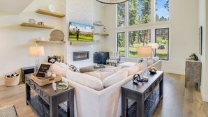 Un salón espacioso con un sofá modular grande, una chimenea y vistas al exterior a través de ventanas amplias.