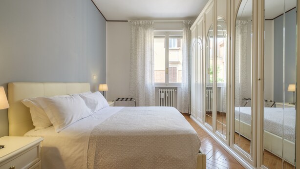 A bedroom with a large bed, a nightstand, a radiator, and a view through a glass door. - San Pietro House by Studio Vita (Bologna)