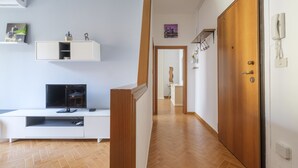 A hallway with a wooden floor, a white entertainment unit with a TV, and a wooden door on the right. - San Pietro House by Studio Vita (Bologna)