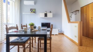 A dining area with a wooden table and chairs, a television, and a plant on the wall. - San Pietro House by Studio Vita (Bologna)