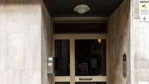 A building entrance with a glass door, a metal door handle, a security keypad, and a doormat. - San Pietro House by Studio Vita (Bologna)