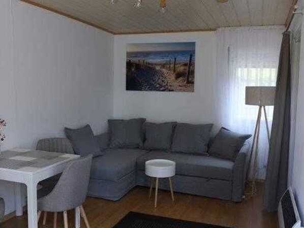Ein modernes Wohnzimmer mit einem grauen Ecksofa, einem kleinen runden Tisch und einem Bild mit Strandmotiv.