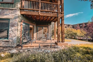 A stone building with a wooden balcony, two chairs, and a small table on the porch.