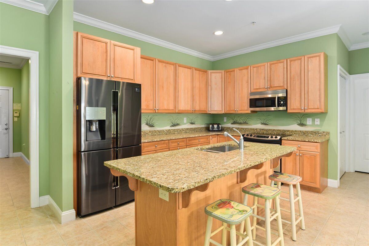 A kitchen with wooden cabinets, stainless steel appliances, a granite countertop, and a small island with stools.