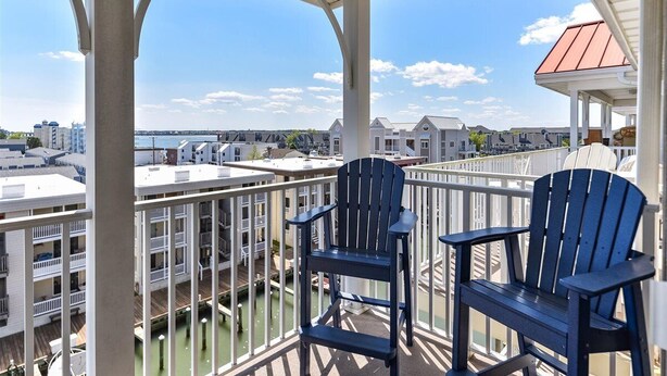 A balcony with two Adirondack chairs overlooking a marina and cityscape.