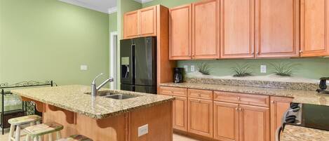 Eine Küche mit Holzausstattung, einer Granitarbeitsplatte, einem Edelstahlkühlschrank und einer Bar mit Barhocker.