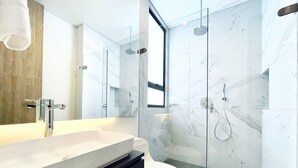 A modern bathroom with a large mirror, a white sink, a toilet, and a glass-enclosed shower area.