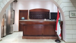 A reception desk with a wooden counter, a clock, and a flag. - Rami Hotel (Falougha-Khalouat)