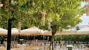 An outdoor wedding venue with round tables and white chairs, surrounded by trees and covered with white canopies. - Rami Hotel (Falougha-Khalouat)