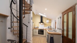 Una cocina moderna con escalera de madera, horno empotrado y una pequeña zona de comedor.