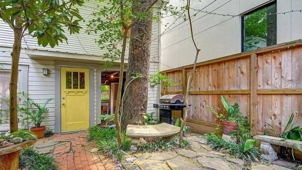 A backyard with a yellow door, a barbecue grill, and a wooden fence.