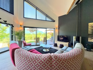 A modern living room with a large TV, comfortable seating, and a view of a garden. - Magnificent villa with heated pool air conditioning (Viviers-du-Lac)