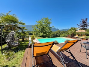 A pool with a wooden deck, two lounge chairs, a hanging chair, and a view of mountains. - Magnificent villa with heated pool air conditioning (Viviers-du-Lac)