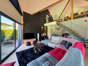 A modern living room with a large TV, a sofa, a coffee table, and a staircase leading to an upper level. - Magnificent villa with heated pool air conditioning (Viviers-du-Lac)