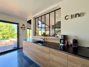 Une cuisine moderne dotée d’un grand îlot central, d’un évier intégré et d’une fenêtre donnant sur une terrasse.