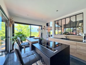 A modern kitchen with a central island, large windows, and a view of greenery.