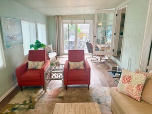 Sala de estar com duas poltronas vermelhas, um sofá bege e uma mesa de centro de vidro, com vista para o pátio exterior.