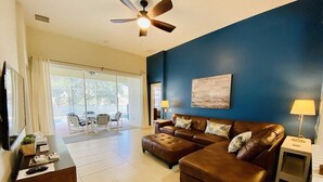 A living room with a brown leather sofa, a coffee table, a TV, and a ceiling fan.