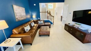 A living room with a brown leather sofa, a white side table, a wooden cabinet, and a flat-screen TV.