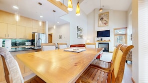 A modern kitchen with wooden cabinets, a stainless steel refrigerator, and a dining area with a wooden table and chairs.