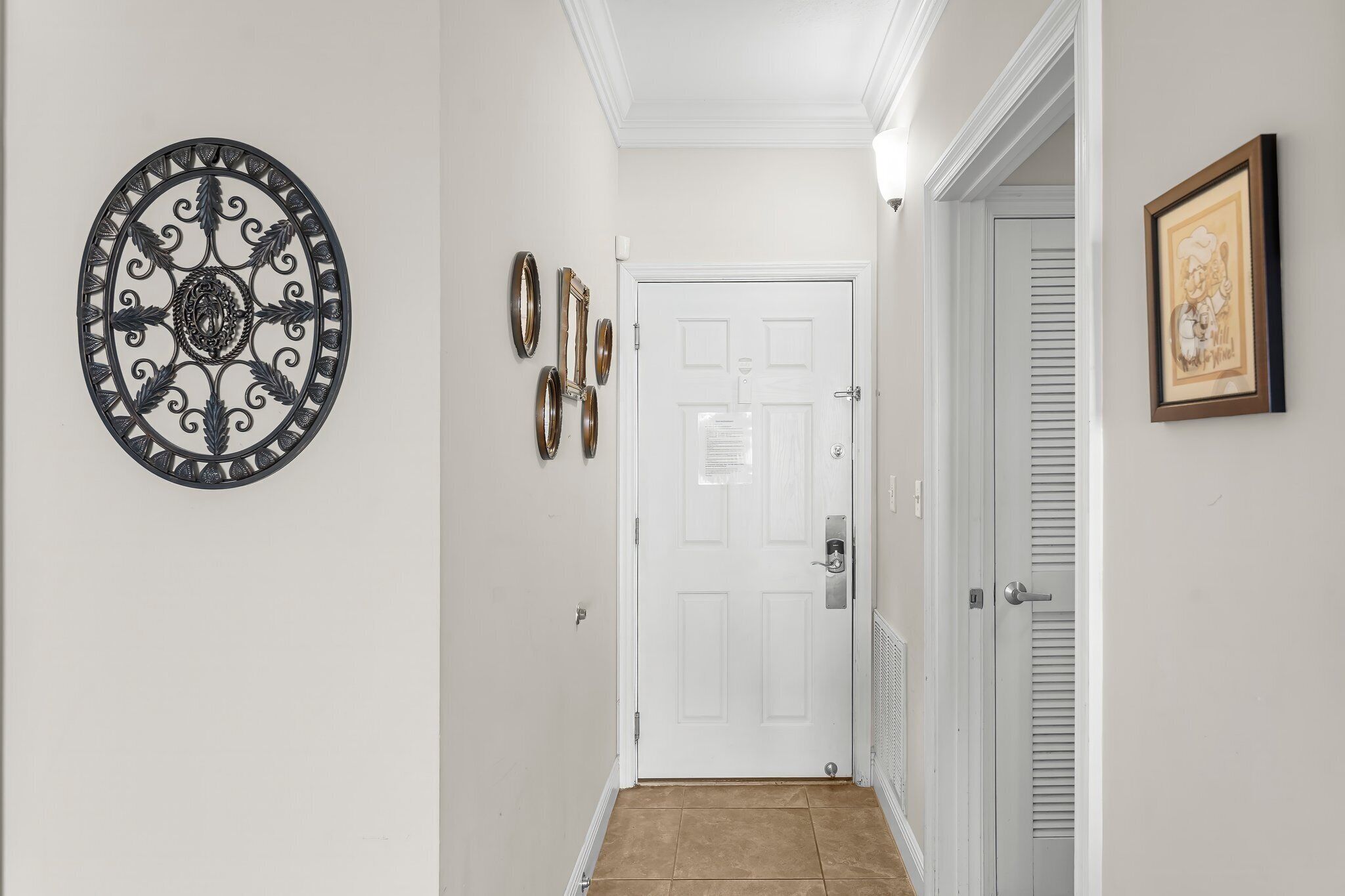A hallway with a white door, a decorative metal wall piece, and a framed picture.