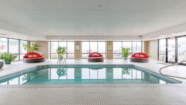 Una piscina con tres zonas de estar circulares rojas, ventanas amplias y plantas en macetas.