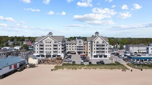 Un hotel frente a la playa con varios balcones, un estacionamiento y una zona de arena.