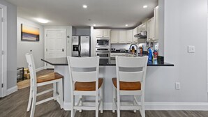 Una cocina moderna con armarios blancos, una isla central y un comedor con sillas blancas.
