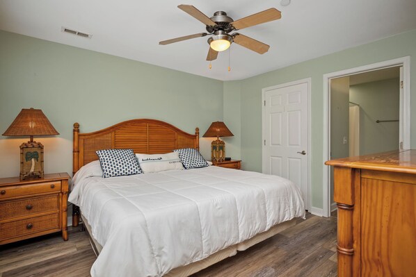 Un dormitorio con una cama de madera, dos mesitas de noche con lámparas, un ventilador de techo y una puerta.